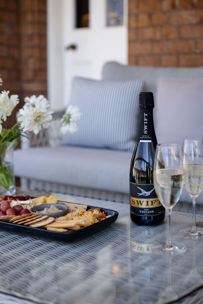 Bottle of sparkling wine with two glasses and cheese platter on outdoor table
